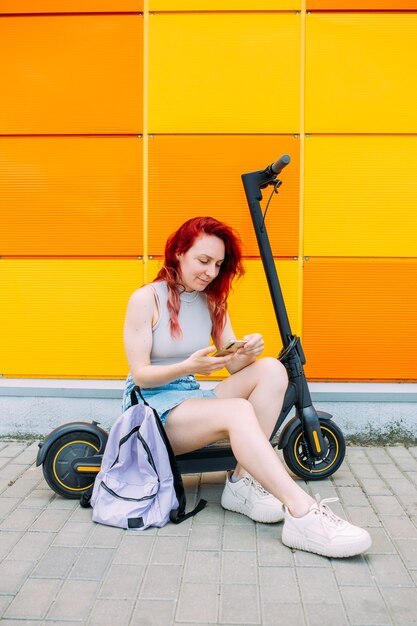Женщина использует смартфон и электрический скутер летом в городе