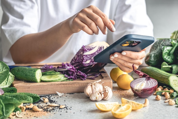 A woman uses a smartphone in the kitchen while preparing a vegetable salad