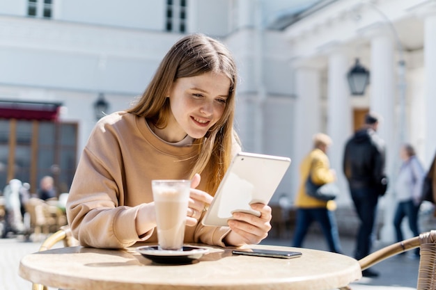 A woman uses a tablet sitting in a summer cafe on the street\
online training a teenager communicates