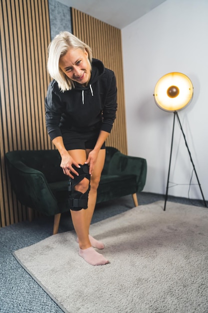 Photo woman using a black knee support brace at home to recover from injuries