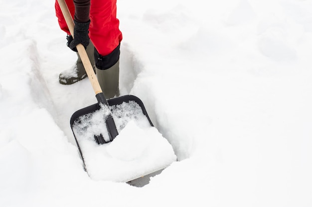 Woman using black plastic shovel with a wooden handle makes the path in the snow