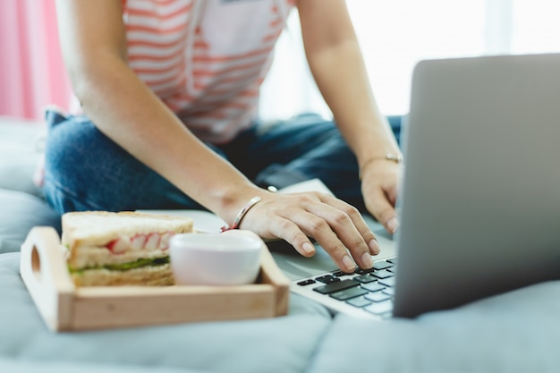 Woman using computer and having breakfast in bed for self-quarantine, social distancing, staying and working at home