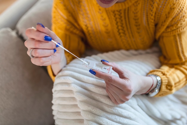 Woman using cotton swab while doing coronavirus PCR test at home. Woman using coronavirus rapid diagnostic test. Young woman at home using a nasal swab for COVID-19.