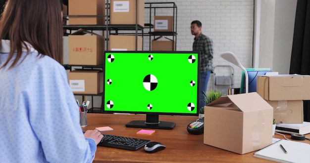 녹색 스크린 컬러 디스플레이가 있는 데스크톱 컴퓨터를 사용하는 여성 마분지 상자로 가득 찬 유통 창고에서 일하는 여성과 남성