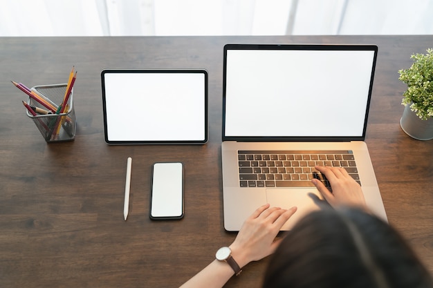 Woman using digital laptop and tablet with phone on the table in house. Blank screen for advertising