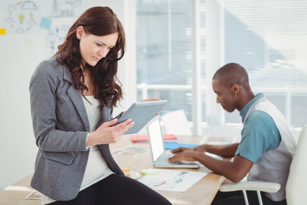 Woman using digital tablet while sitting on desk with man working 