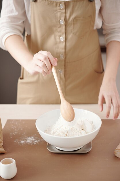 自宅で作っているペストリーの小麦粉を測定するために電子はかりを使用している女性