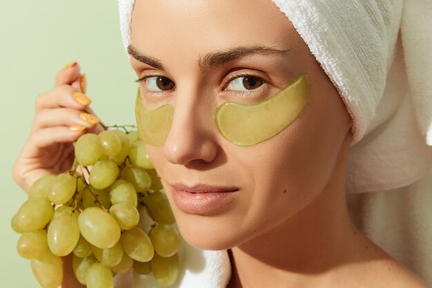 Foto donna che utilizza bende per gli occhi a base di vinaccioli su sfondo verde pastello