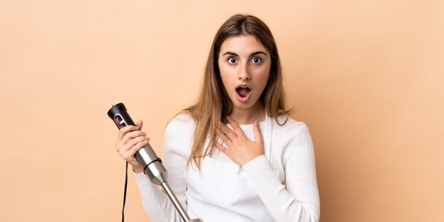 Woman using hand blender over isolated surprised and shocked while looking right