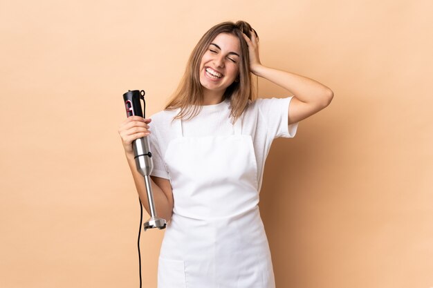 Woman using hand blender over isolated wall laughing