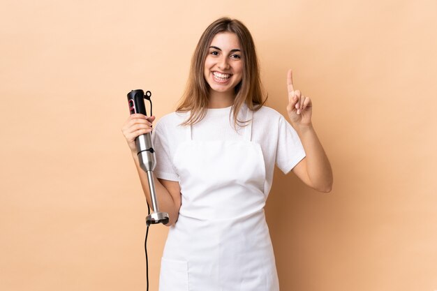 Woman using hand blender over isolated wall pointing up a great idea