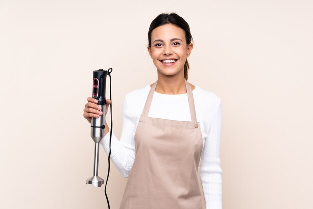 Woman using hand blender over isolated wall smiling a lot