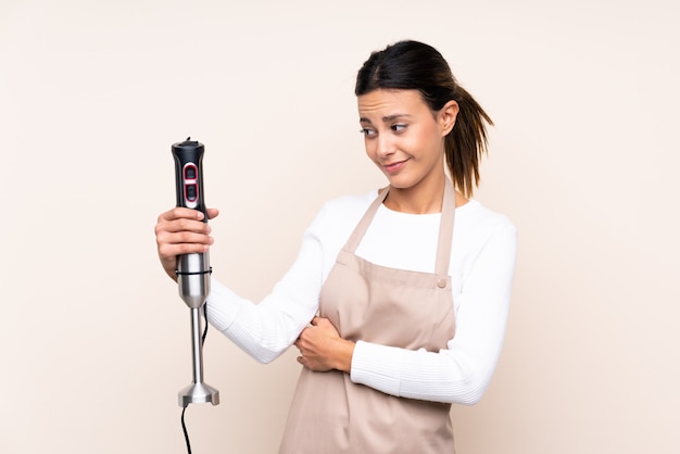 Woman using hand blender over wall with sad expression