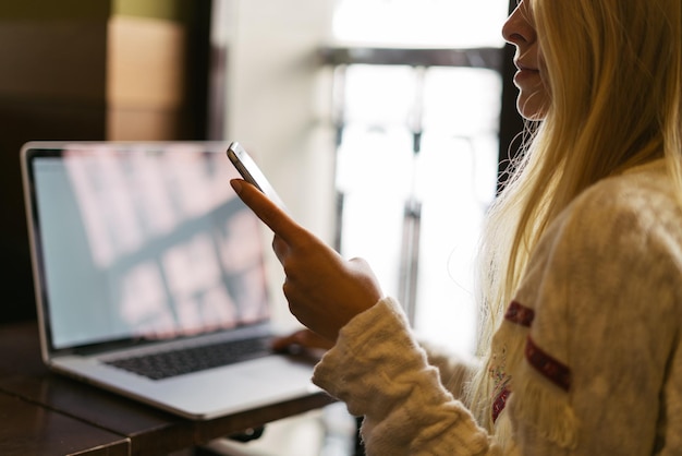 Woman using her cellpohone with computer in the background.