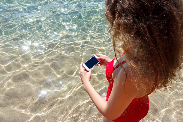 海の背景に彼女の携帯電話を使用している女性