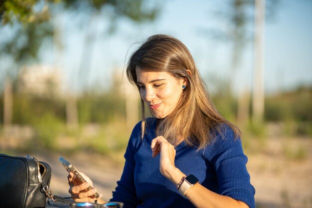 Foto donna che usa il suo cellulare e sorride mentre è seduta su un tavolo all'aperto nella natura tecnologia