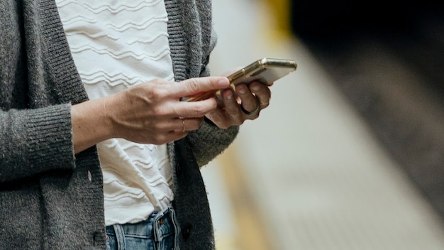 Donna che usa il cellulare mentre aspetta il treno durante la pandemia di coronavirus