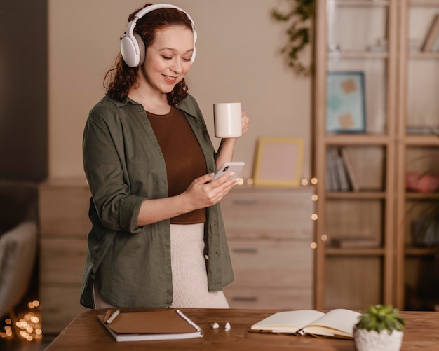 Foto donna che utilizza il suo smartphone e le cuffie a casa mentre beve il caffè