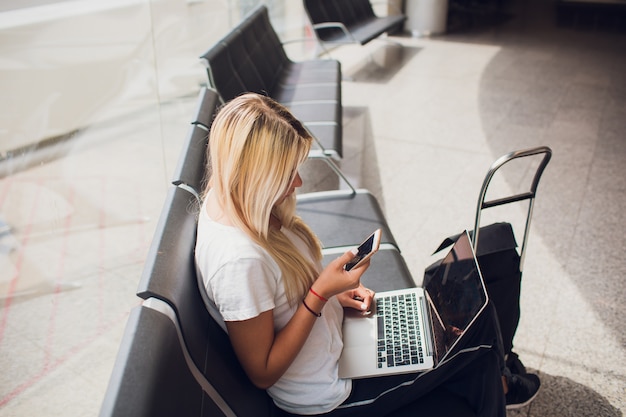 휴가 여름 편안한 비행 전송 편안한 여행 수하물 가방과 배낭 앉아 공항 터미널에서 랩톱 컴퓨터를 사용하는 여자.