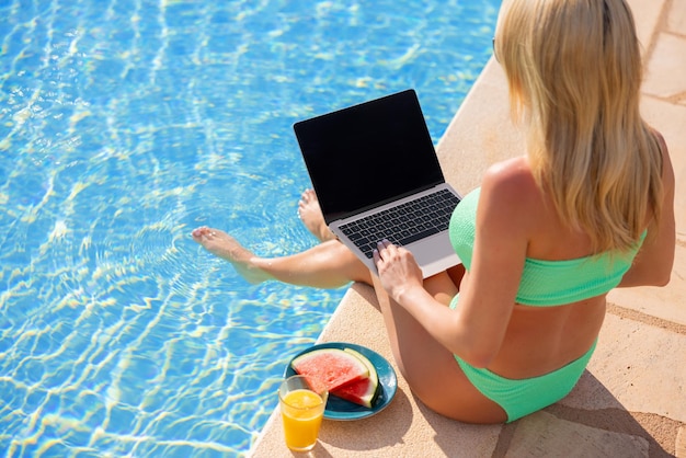 Woman using laptop computer on vacation by the pool