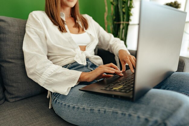 家のソファに座っている間ラップトップコンピュータを使用している女性