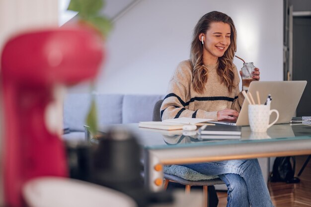 自宅でラップトップを使用し、エコストローでコーヒーを飲む女性