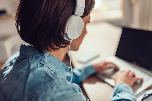 Woman using laptop and listening music on a headphones