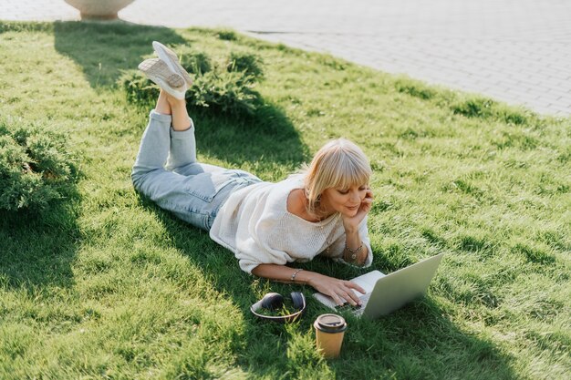 Donna che utilizza laptop sdraiata sull'erba