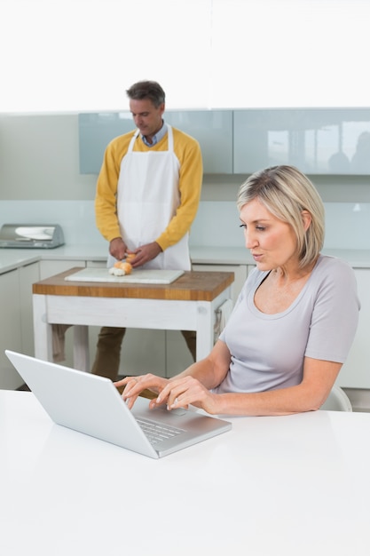 Foto donna che utilizza computer portatile e uomo che taglia le verdure a pezzi