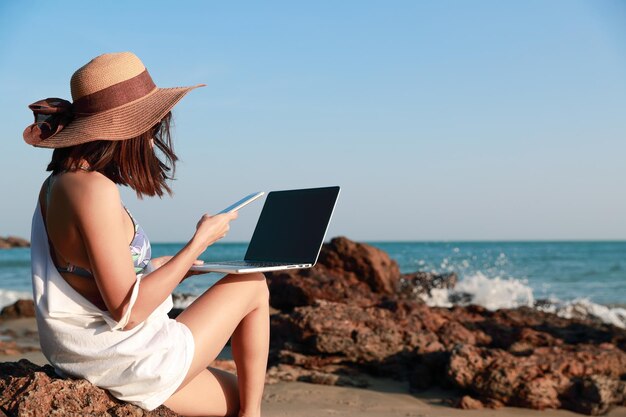 Photo woman using laptop and mobile phone at beach