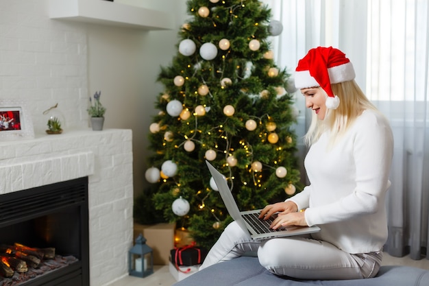 Woman using laptop near Christmas tree.