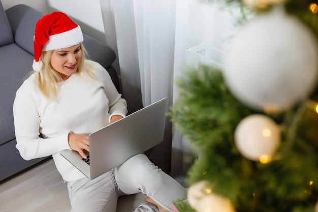 Woman using laptop near Christmas tree.