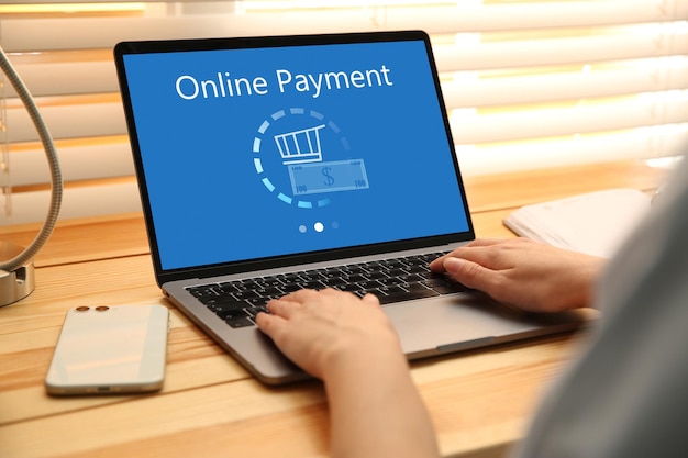 woman using laptop for online payment at wooden table closeup