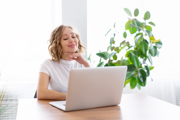 Woman using laptop sitting desk office interior with houseplant