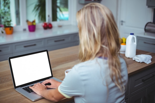 Woman using laptop at table in kitchen