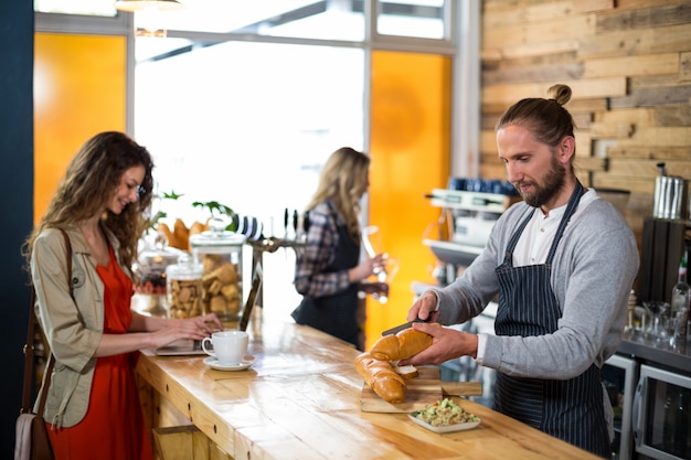 Woman using laptop and waiter cutting bread at counter