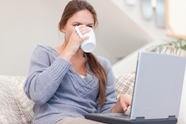 Женщина, используя ноутбук, выпив чашку чая