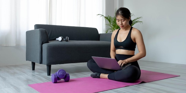 Woman using laptop while exercising at home Female in sportswear sitting on floor and watching exercise video for her workout