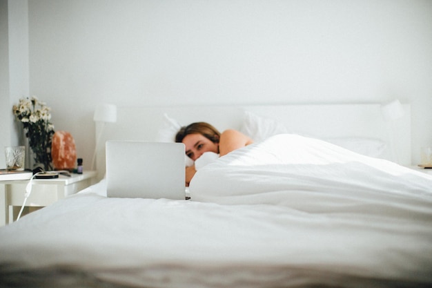 Photo woman using laptop while lying on bed at home