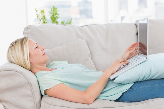 Woman using laptop while lying on sofa