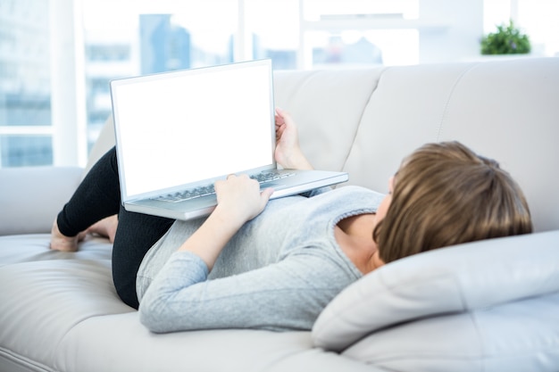 Donna che per mezzo del computer portatile mentre trovandosi sul sofà