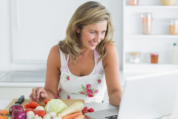 Donna che utilizza computer portatile mentre si prepara le verdure