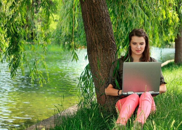 Woman using laptop while sitting on grassy field in park
