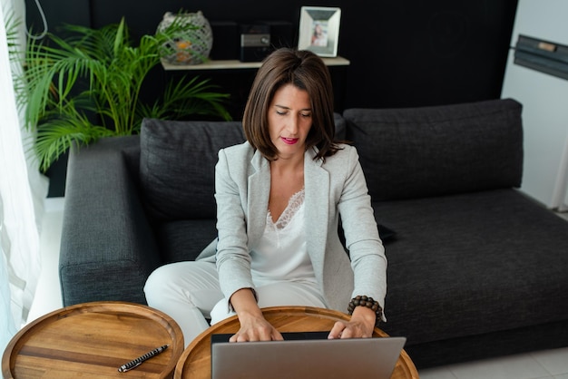 Photo woman using laptop while sitting on sofa at home