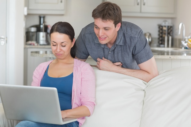 Woman using laptop with man looking on