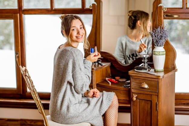 Woman using lipstick at the dressing table near the window at the wooden house during the window time