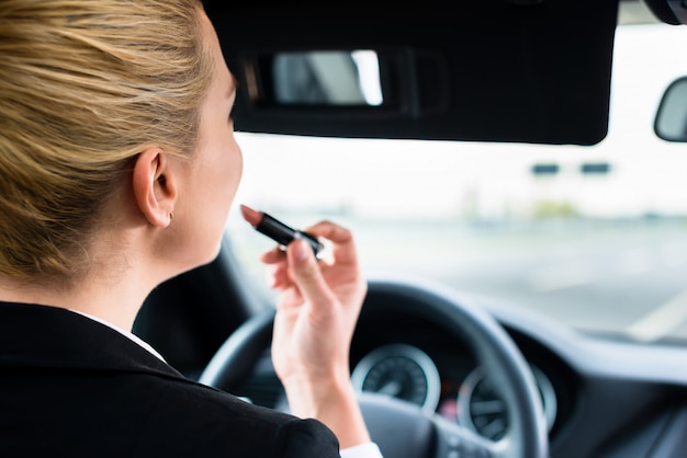 Woman using lipstick while driving her car