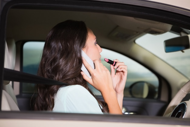 Woman using mirror to put on lipstick while on the phone