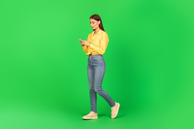 緑の背景の上を歩くインターネットを閲覧する携帯電話を使用している女性