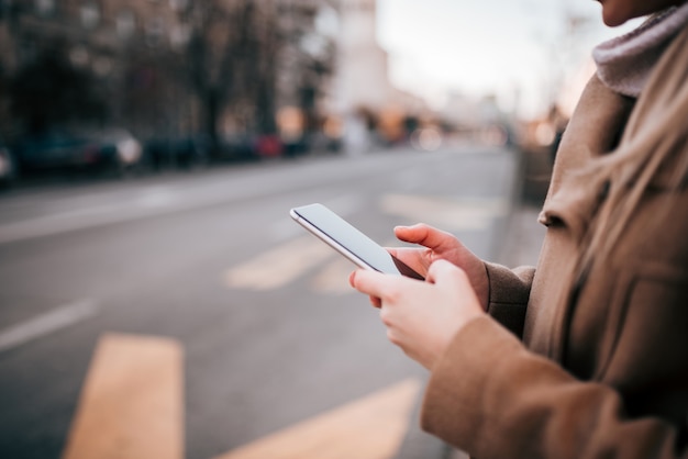 Woman using mobile phone by the city street.